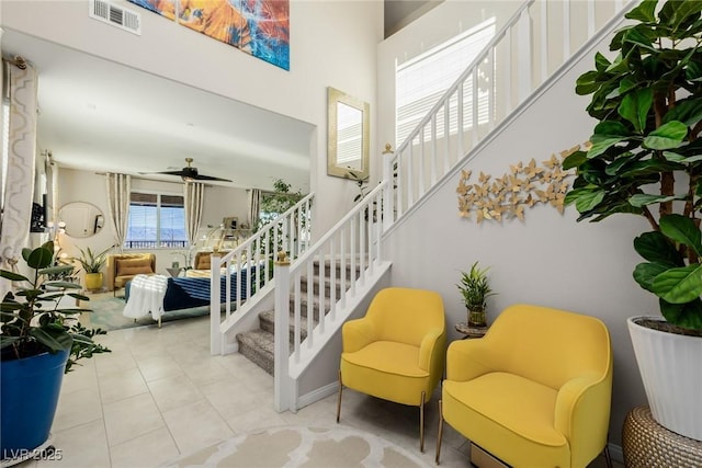 stairs featuring tile patterned floors, visible vents, a towering ceiling, and a ceiling fan