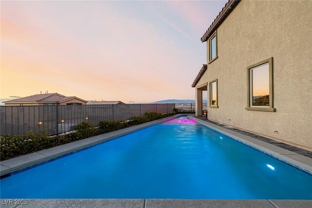 pool at dusk featuring a fenced in pool and a fenced backyard