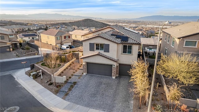 view of front of house with a residential view, roof mounted solar panels, decorative driveway, a garage, and a mountain view