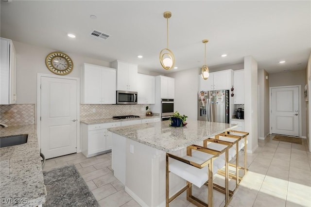 kitchen with visible vents, a sink, light stone counters, a kitchen island, and stainless steel appliances
