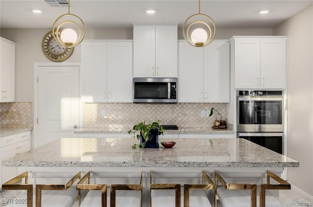 kitchen featuring decorative light fixtures, white cabinetry, stainless steel appliances, and a kitchen bar