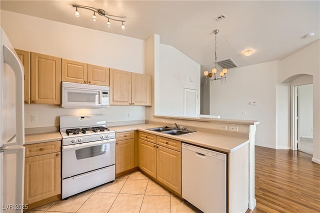 kitchen featuring a sink, white appliances, arched walkways, and light brown cabinetry