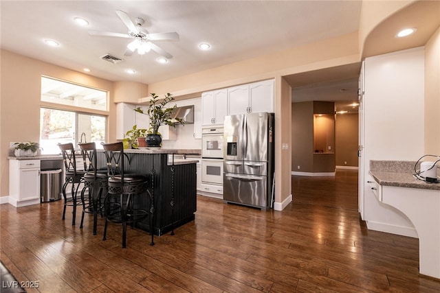 kitchen with stainless steel fridge with ice dispenser, ceiling fan, a kitchen breakfast bar, white cabinetry, and visible vents