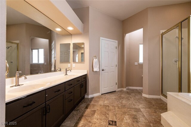 bathroom with a shower stall, double vanity, a sink, and baseboards