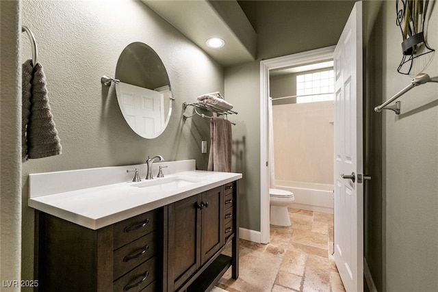 full bath with toilet, stone tile floors, vanity, and shower / washtub combination