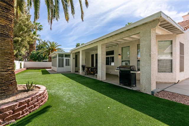 rear view of property with a sunroom, a patio area, a lawn, fence, and stucco siding
