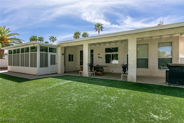 back of house featuring a yard, a patio, stucco siding, and a sunroom