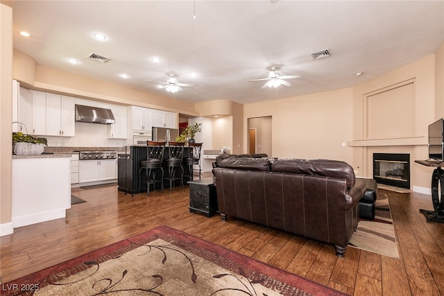 living room featuring ceiling fan, visible vents, and dark wood-style flooring