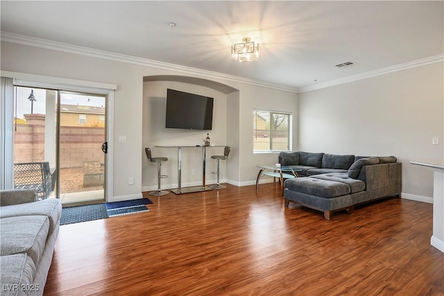 living area with visible vents, baseboards, wood finished floors, and crown molding