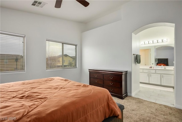bedroom with a ceiling fan, visible vents, arched walkways, ensuite bathroom, and light carpet