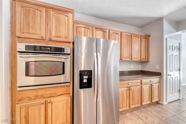 2528 Flodden St, Henderson, NV 89044 - kitchen featuring light brown cabinets, a textured ceiling, light tile patterned flooring, dark stone counters, and appliances with stainless steel finishes