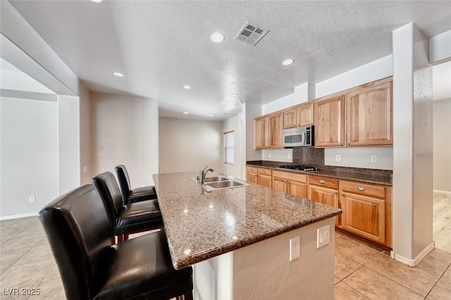 2528 Flodden St, Henderson, NV 89044 - kitchen with visible vents, light tile patterned floors, a sink, stainless steel microwave, and dark stone counters