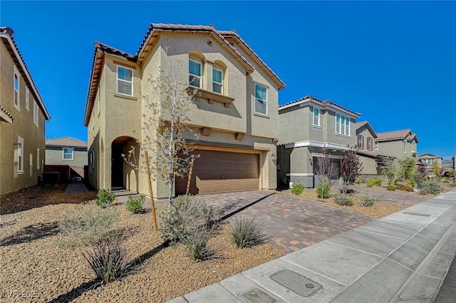 mediterranean / spanish-style house featuring stucco siding, a tile roof, decorative driveway, a residential view, and an attached garage