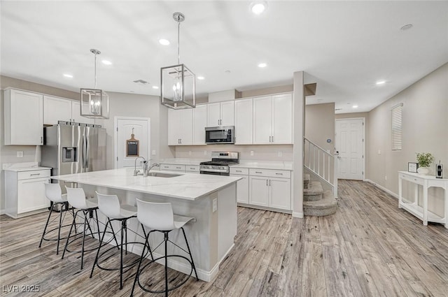 kitchen featuring light wood-style flooring, appliances with stainless steel finishes, white cabinets, and a sink