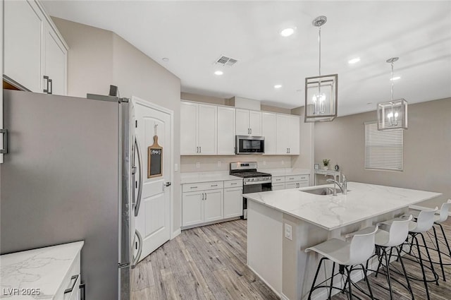 kitchen featuring visible vents, a sink, light stone counters, appliances with stainless steel finishes, and light wood finished floors