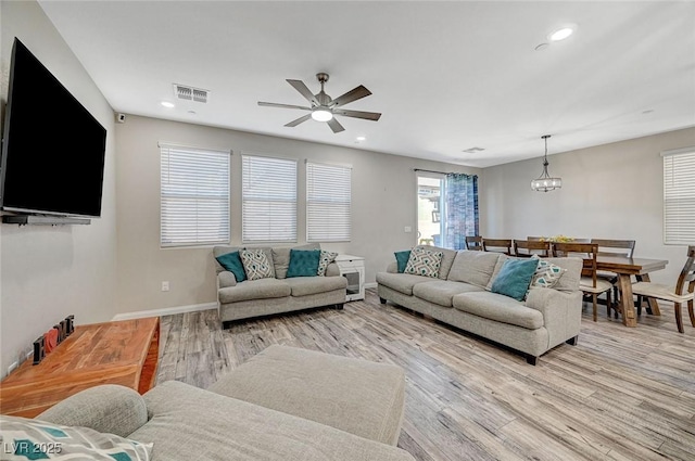 living area with visible vents, light wood-style flooring, ceiling fan with notable chandelier, recessed lighting, and baseboards