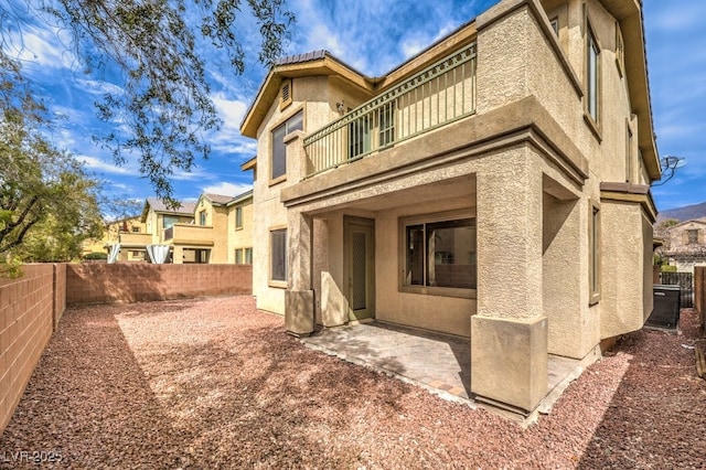 back of house featuring stucco siding, a balcony, a fenced backyard, and a patio