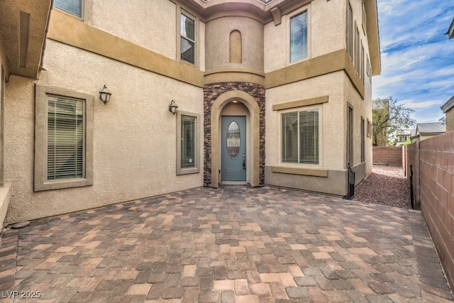 doorway to property with stucco siding, a patio area, and fence
