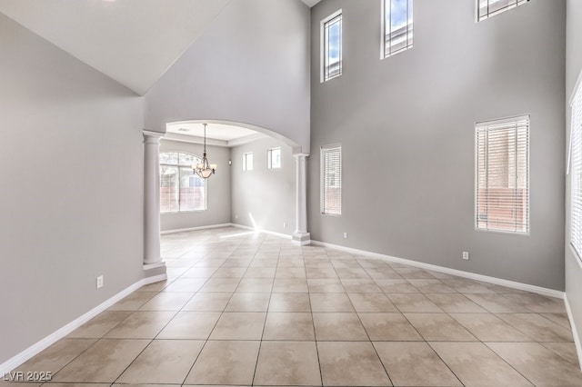 unfurnished living room featuring a towering ceiling, decorative columns, light tile patterned flooring, a chandelier, and arched walkways