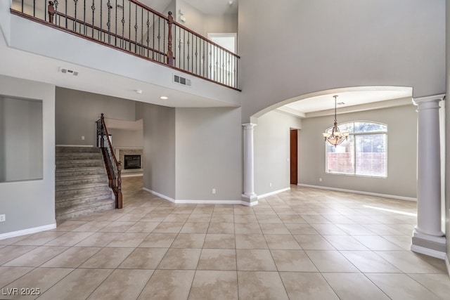 unfurnished living room with a chandelier, a towering ceiling, tile patterned floors, baseboards, and ornate columns