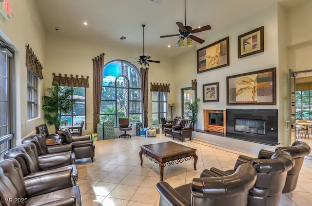 tiled living room featuring ceiling fan, a glass covered fireplace, recessed lighting, and a towering ceiling