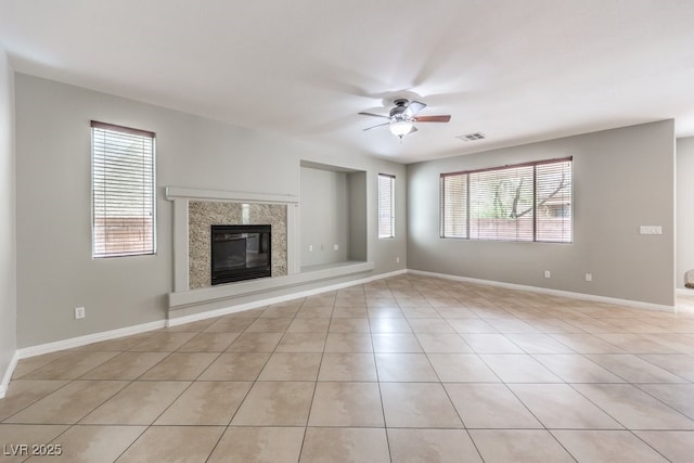 unfurnished living room featuring ceiling fan, healthy amount of natural light, light tile patterned flooring, and a premium fireplace