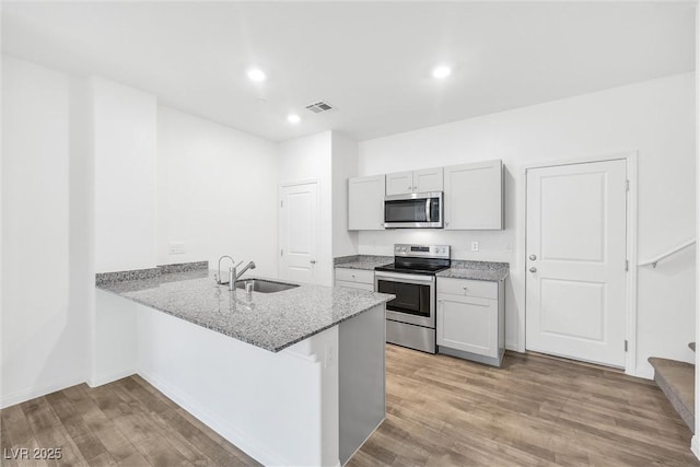 4125 Venus Falls Ave, North Las Vegas, NV 89084 - kitchen featuring appliances with stainless steel finishes, a peninsula, light stone counters, light wood-type flooring, and recessed lighting