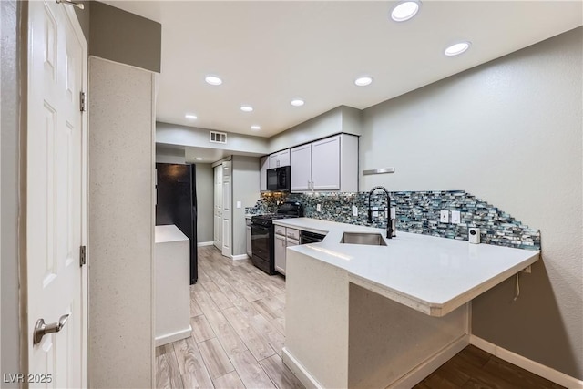 kitchen with light wood finished floors, visible vents, backsplash, black appliances, and a sink