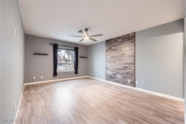 unfurnished room featuring an accent wall, wood finished floors, baseboards, and ceiling fan
