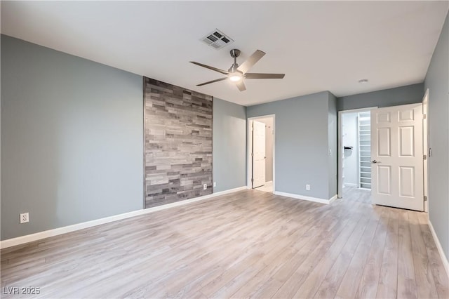 empty room with a ceiling fan, visible vents, baseboards, light wood-style floors, and an accent wall