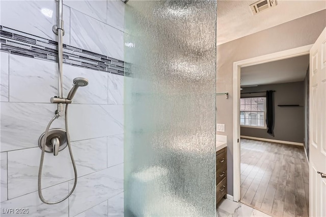 bathroom with visible vents, tiled shower, vanity, and baseboards