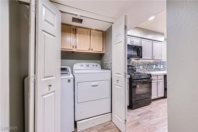 laundry room featuring washer and dryer, cabinet space, light wood-type flooring, and a textured wall