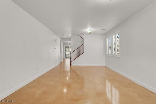 empty room with a healthy amount of sunlight, baseboards, stairway, and concrete floors