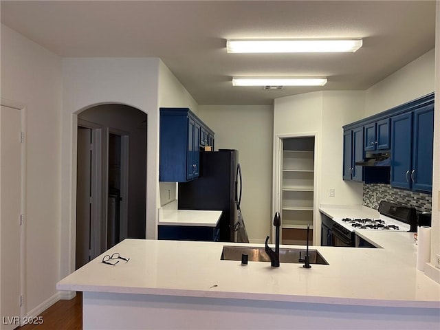 kitchen featuring blue cabinets, under cabinet range hood, white gas range oven, and a sink