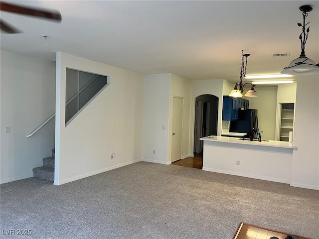 unfurnished living room with visible vents, baseboards, arched walkways, stairs, and dark colored carpet
