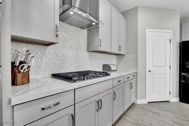 kitchen with stainless steel gas cooktop, light stone counters, wall chimney range hood, and backsplash