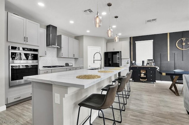 kitchen with wall chimney range hood, double oven, visible vents, and a sink