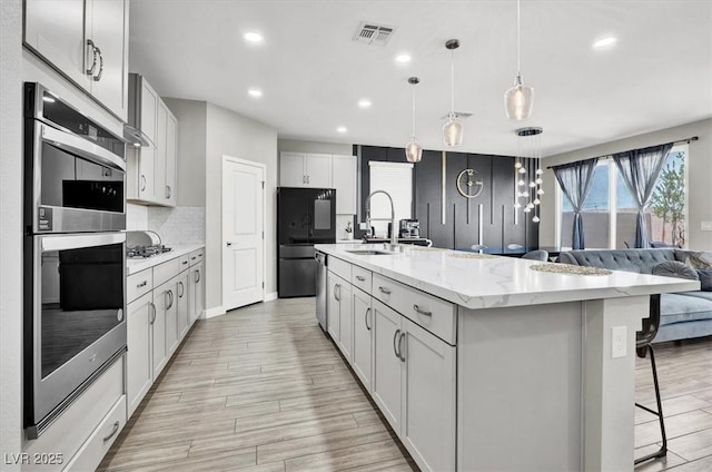 kitchen featuring tasteful backsplash, a breakfast bar, stainless steel double oven, visible vents, and smart refrigerator