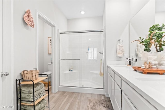 full bath with a stall shower, wood finished floors, double vanity, and toilet