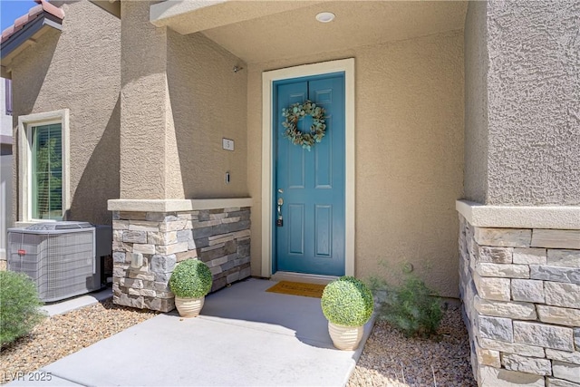 view of exterior entry featuring stucco siding, cooling unit, and stone siding