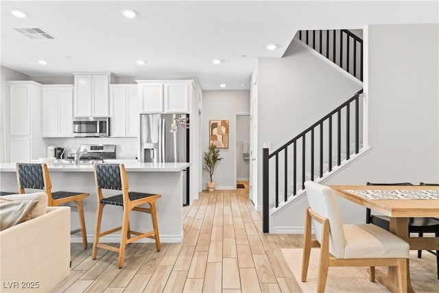 kitchen featuring stainless steel appliances, light countertops, decorative backsplash, white cabinets, and light wood-type flooring
