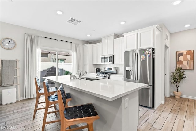 kitchen featuring appliances with stainless steel finishes, wood finish floors, a sink, white cabinets, and recessed lighting