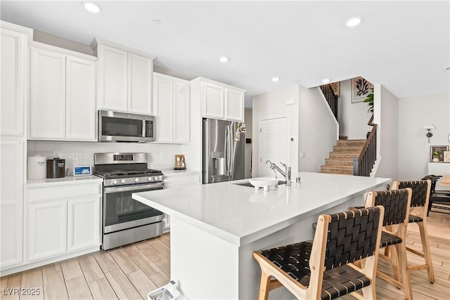 kitchen featuring appliances with stainless steel finishes, a sink, a breakfast bar, light countertops, and a kitchen island with sink