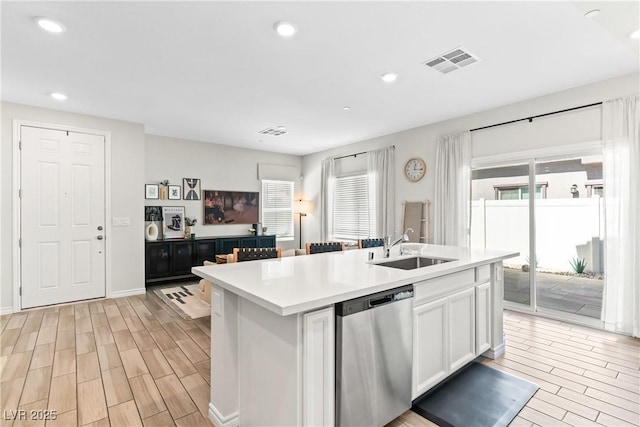 kitchen featuring dishwasher, a sink, wood tiled floors, white cabinets, and a center island with sink