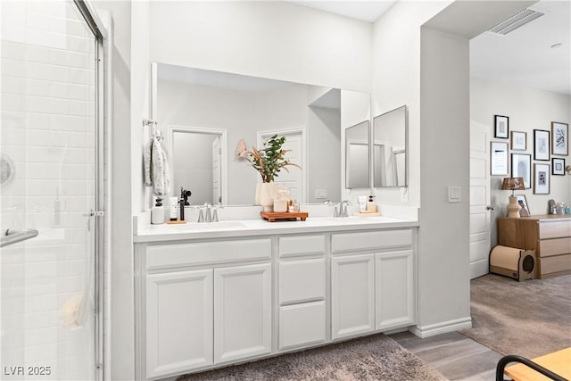 bathroom with a tile shower, double vanity, and wood finished floors