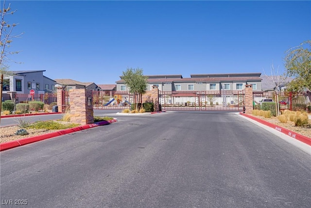 view of asphalt street with a residential view, a gated entry, curbs, and a gate