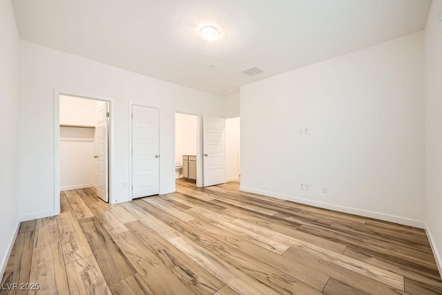 unfurnished bedroom with a closet, light wood-style flooring, baseboards, visible vents, and a walk in closet