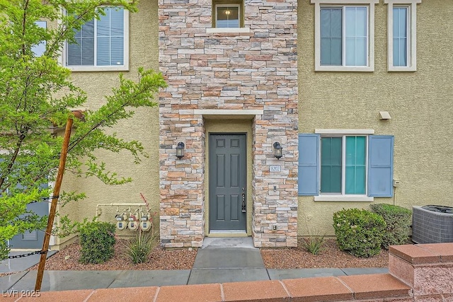 property entrance featuring stone siding, stucco siding, and cooling unit
