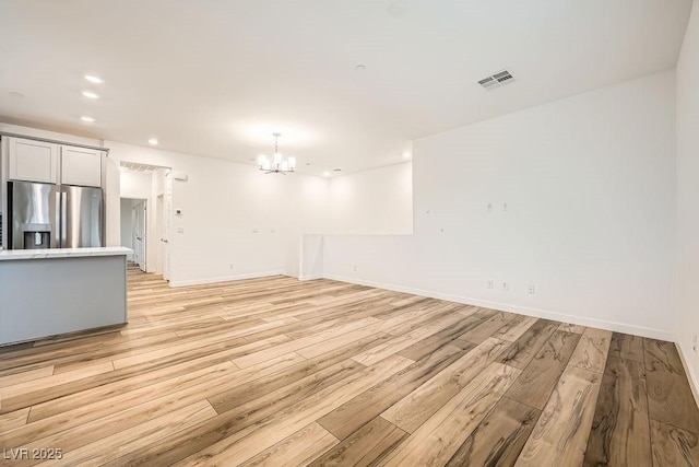 unfurnished living room with a chandelier, light wood-style flooring, baseboards, and recessed lighting