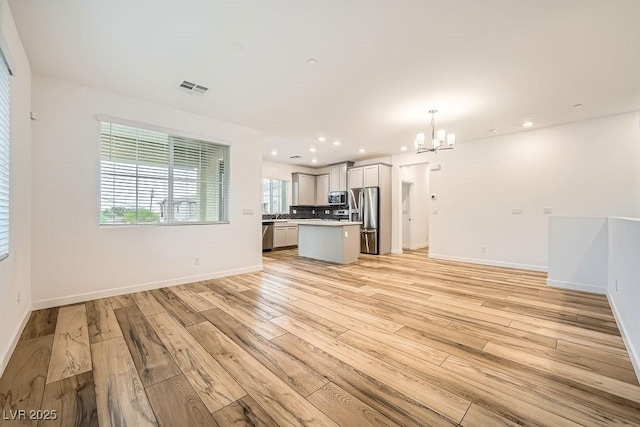 unfurnished living room featuring a chandelier, light wood finished floors, baseboards, and visible vents
